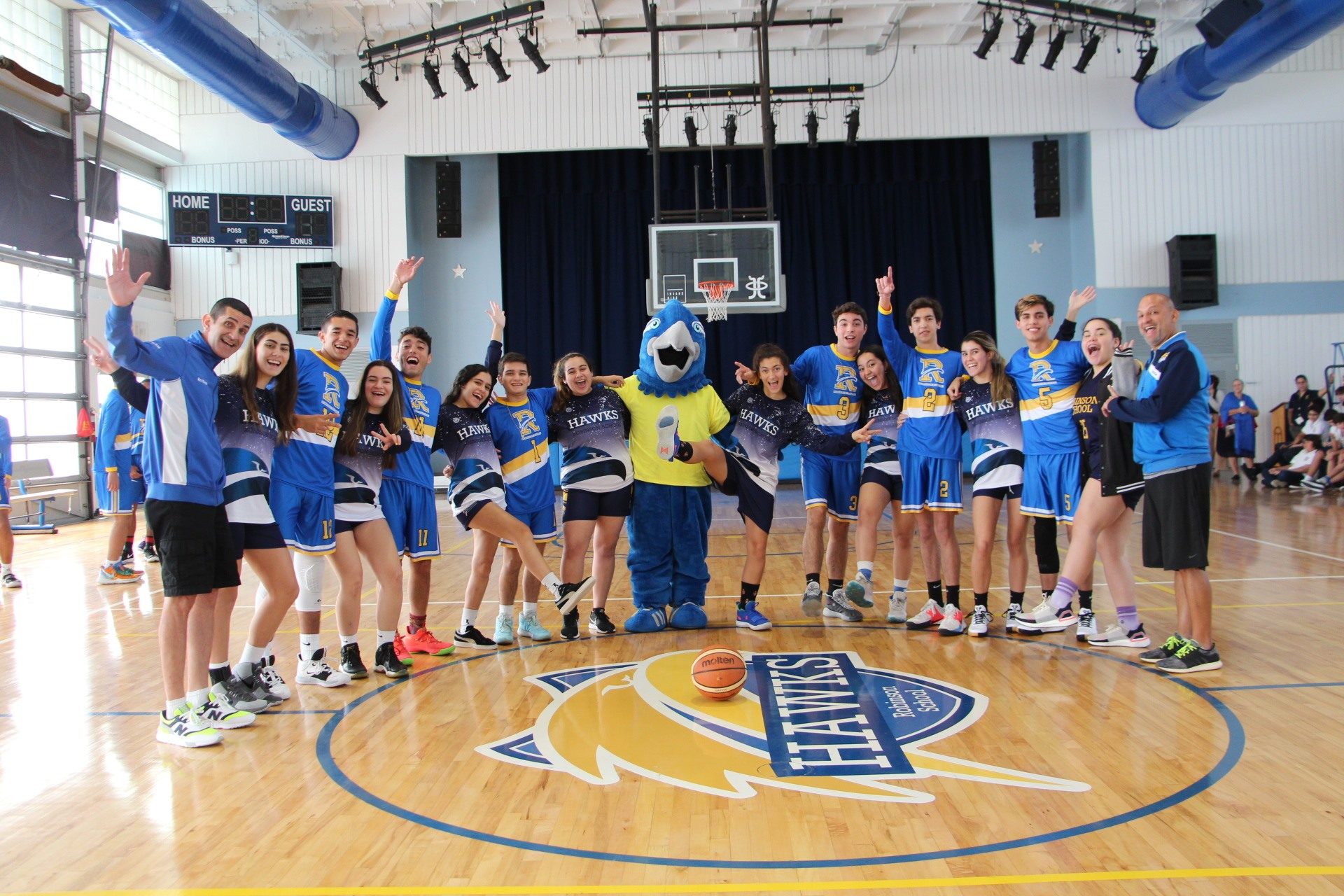 The varsity female and male basketball teams in full uniform pose with the Hawk mascot, along with their athletic coaches.