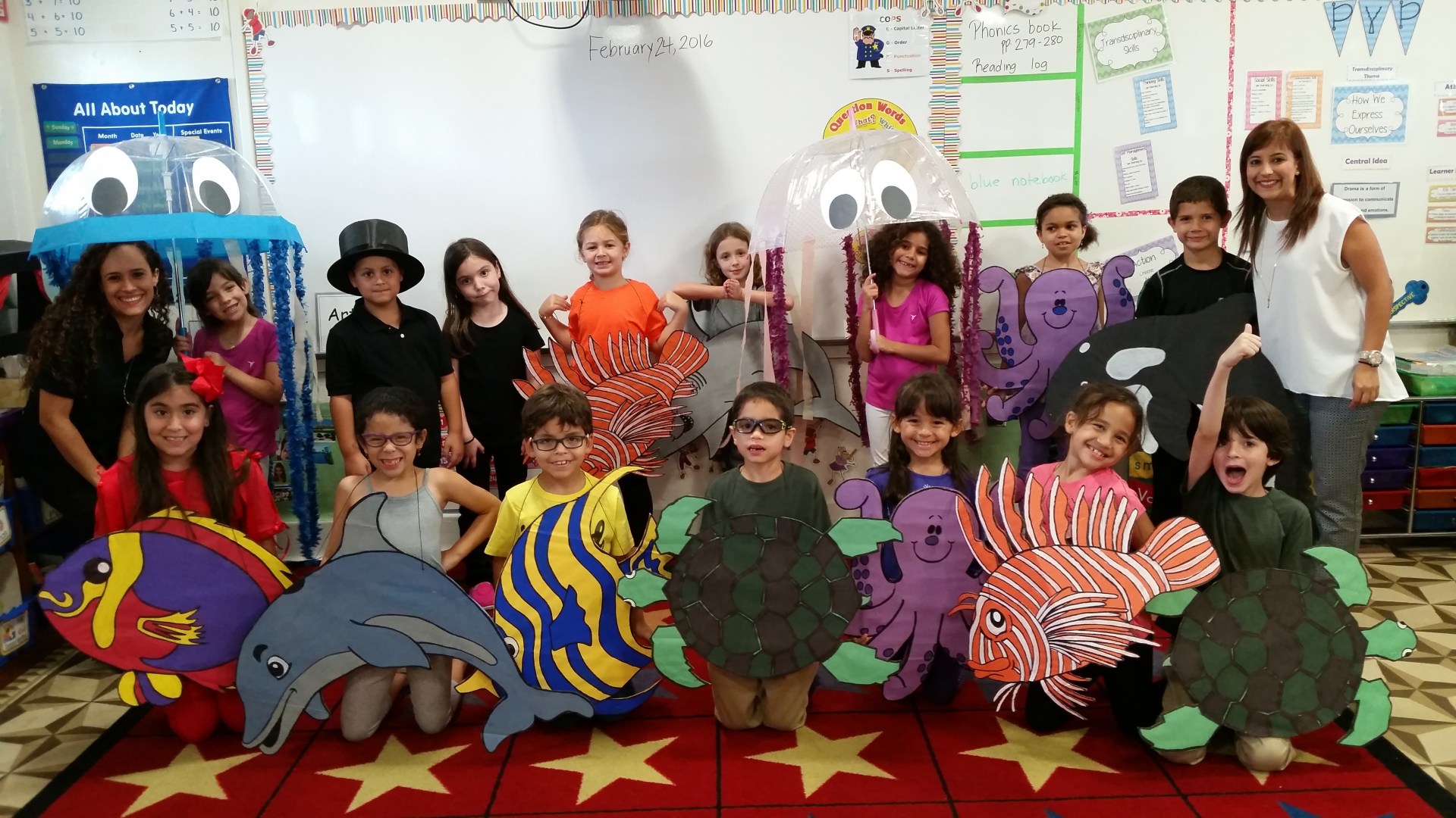 An Elementary school classroom shows off their homemade multicolored sea creature costumes, with their two teachers at the ends of each group.