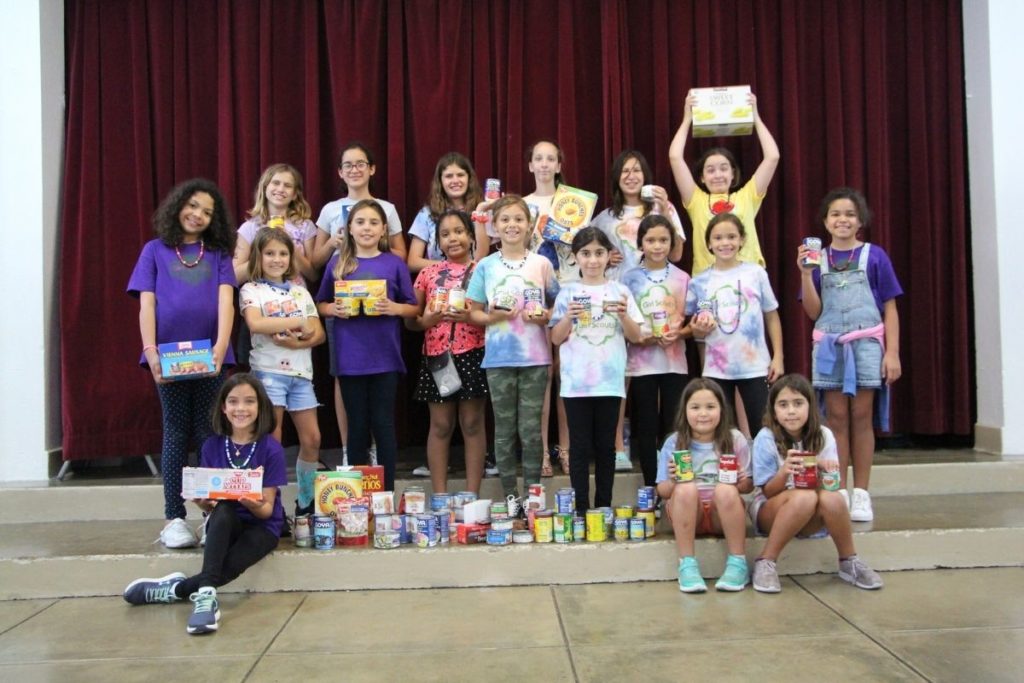 A group of female Robinson School elementary students wearing shades of tie-dye and purple show off the amount collected in their food drive.