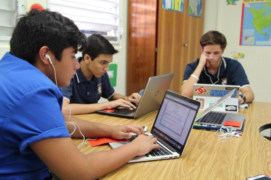 Three male students are busy on their laptops while they work on their online coursework.