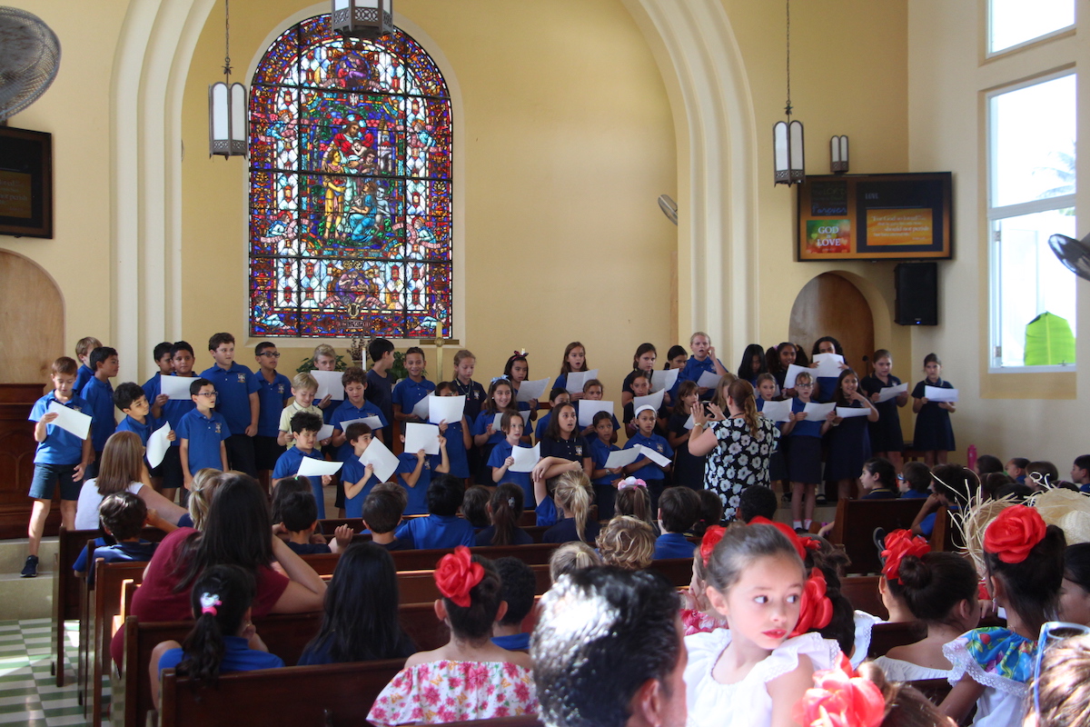 Students in blue Robinson shirts sing in a choir formation at the front of the school's chapel, with their teacher leading them in front.