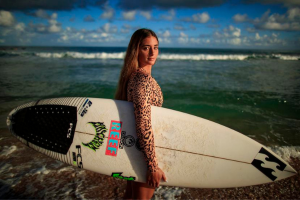 Havanna Cabrero Carrion holding her surfboard in front of the ocean.