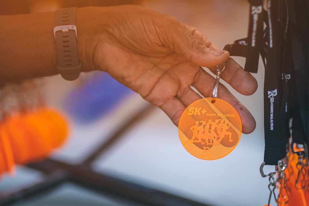 A orange transparent plastic medal with a black lanyard for all 5K Hawk Walk/Run participants.