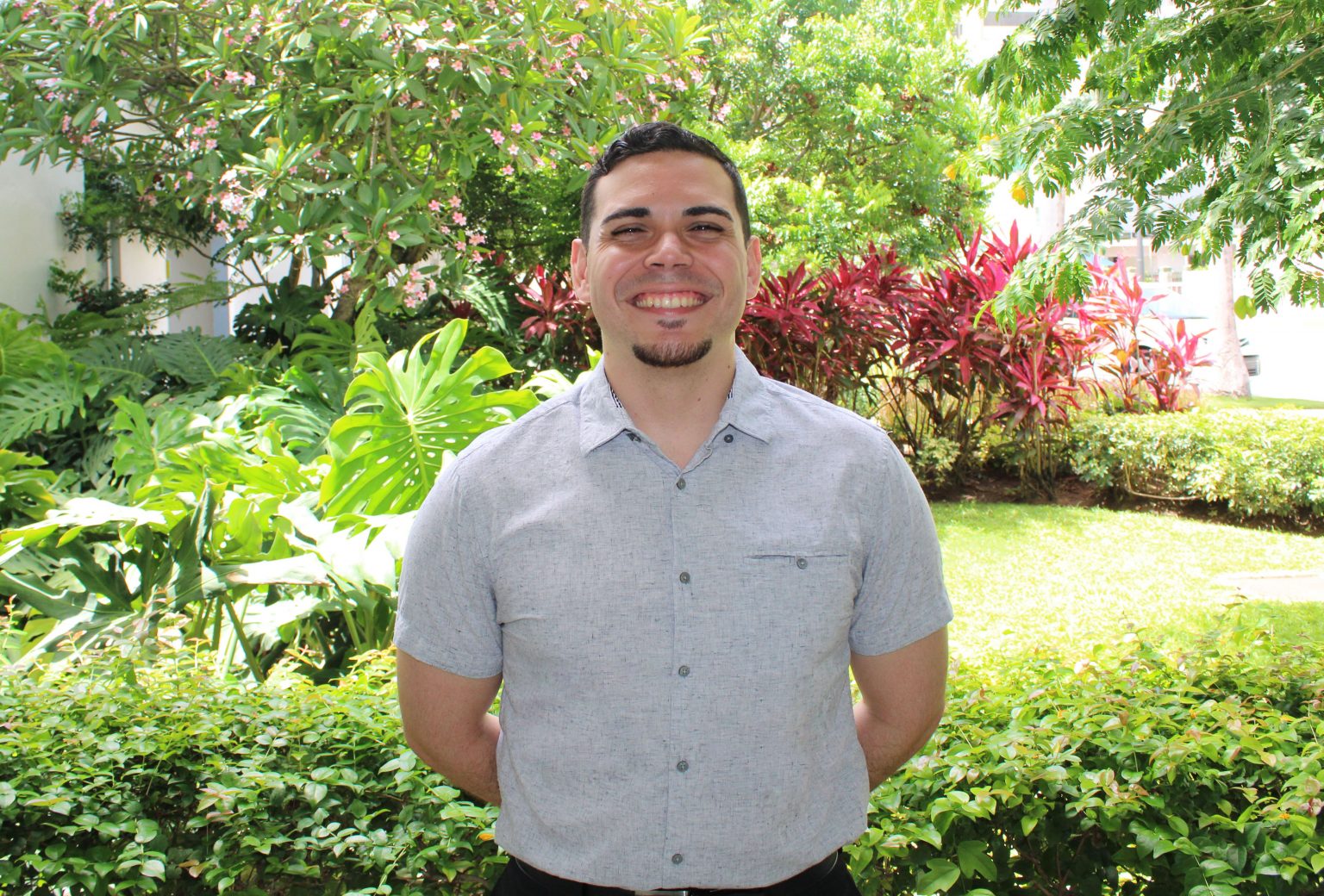 Elementary School Division Head Bradly Rivera stands in front of school greenery while smiling and wearing a grey button up shirt.